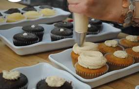 Vanilla icing is being applied to a vanilla cupcake.