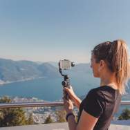A woman filming with cell phone and gimbal in the mountains over Lake Maggiore