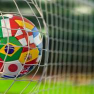 A soccer ball with the flags of countries from around the world, hits the net of a goal.