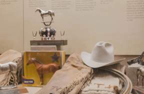 Cowboy hat, chaps, horse trophy, horse toy in case at the American Quarter Horse Museum