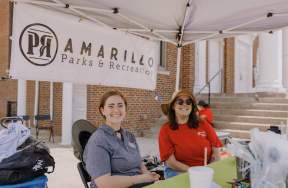 Two young women sitting in front of a Amarillo Parks & Recreation Sign