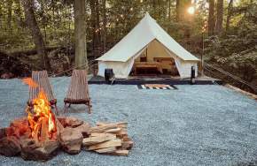 A glamping tent with a lit fire and chairs in front