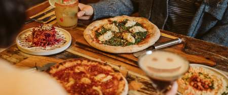 restaurant table filled with pizzas, vegan side dishes and drinks