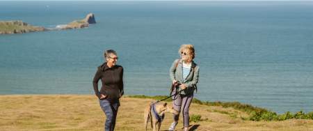 Couple walking their greyhound on coastline