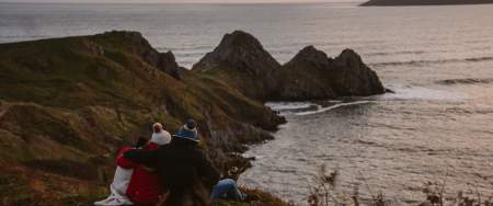 family keeping warm under a blanket with coffee looking out over three cliffs bay