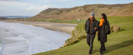Couple walking along rhossili bay coastline