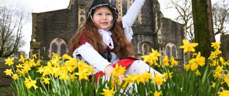A young girl in traditional welsh costume sits in a patch of daffodils