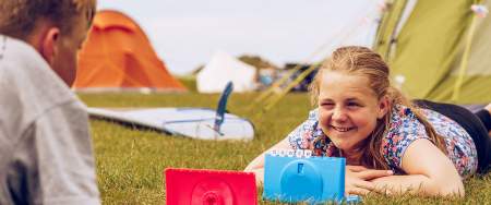 A boy and a girl lying on the grass playing a game on a camp site.
