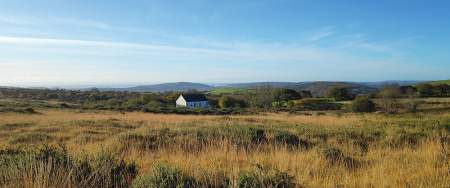 A white chapel in the middle of a gors landscape with Swansea Bay far in the distance.