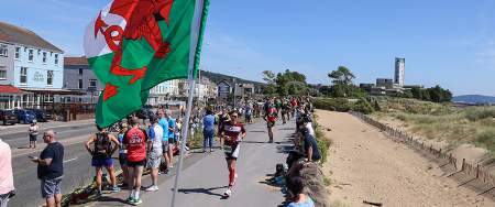 crowd cheering on competitors running along the swansea beach front during the Ironman Swansea event