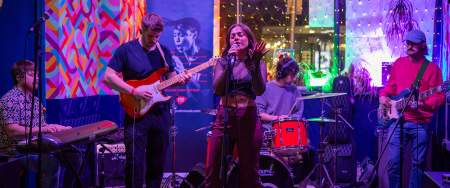 A young five piece band with female singer playing on a colourful stage.