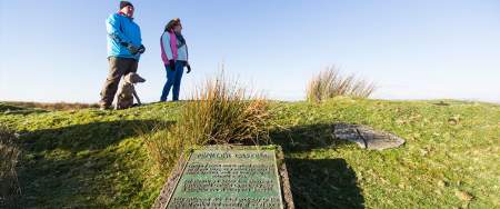 Two walkers and a dog near a plaque