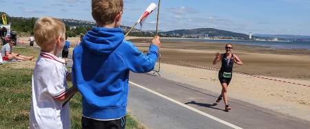 Two young boys cheering on their mum running along the race course waving welsh flags