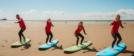 A family of four standing on surf boards on the sand practicing moves.