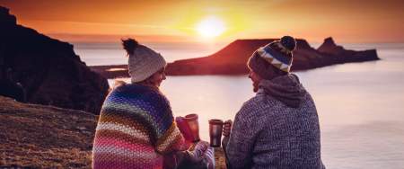 a couple share coffee while the sun sets against worms head