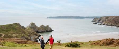 couple holding hands walking along three cliffs bay coastline