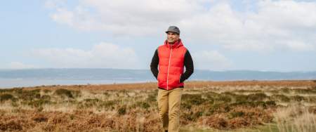 A man in a bright red bodywarmer and flat cap walking on Gower.