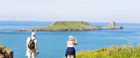 An older couple at Rhossili looking out to Worm's Head. The woman is using binoculars.