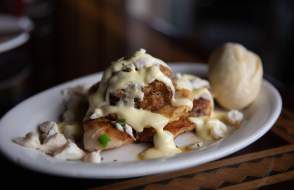 Blackened fish with cream sauce and lump crab meat and a roll on a white oval plate