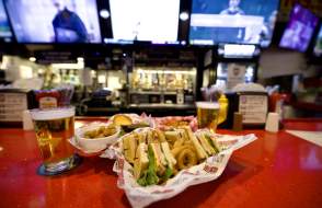 Glass of beer and sandwich platter sitting on bar.