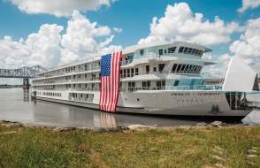 American Cruise Lines' Symphony, a Mississippi riverboat, is in port with an American flag draped down the side.