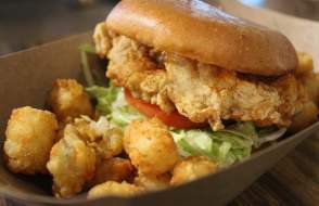 Fried chicken sandwich with lettuce and tomato and a side of tater tots