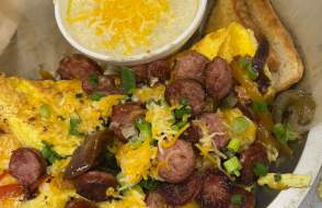 Omelet on a plate with sausage, cheese, green onions, toast and grits topped with cheese