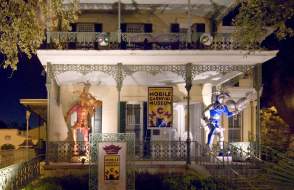 Historical, white house with iron columns and trim, two Mardi Gras Jesters on the porch
