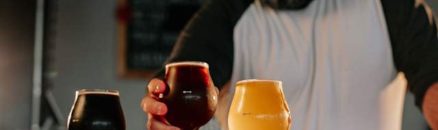 A bartender sets down a glass of beer in a beer flight featuring a dark beer, amber beer, and wheat beer.