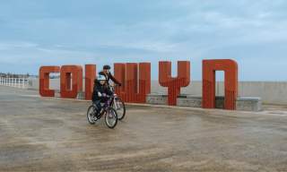 Cyclists going past the Colwyn sign