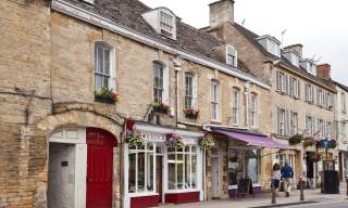 A couple walking past shops with pretty frontages and hanging baskets in Chipping Norton town centre
