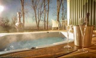 Hot tub bath at the Hilly Huts on FArncombe Estate. Steam rising from tub with bottle of sparkling wine, glasses and chimnea in background