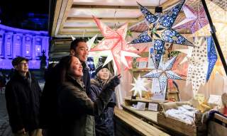 A group of people look at star lanterns in a wooden chalet at Blenheim Palace Chrsitmas Market
