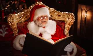 Santa sits in an ornate chair reading a book