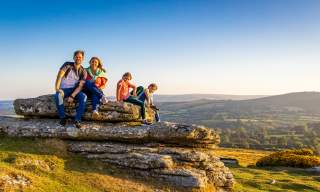 a family of two adults and two children sitting on a flat rock in Dartmoor with spectacular view behind them