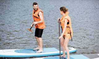 A man and a women are paddleboarding wearing orange life jackets