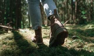 Close-up of a person wearing brown boots and blue jeans walking on a sunlit, moss-covered forest floor, conveying a sense of adventure and tranquility.