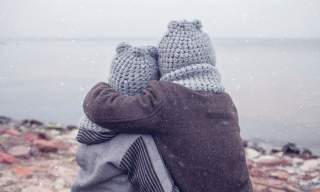 two children in hats having a hug on a wintery beach
