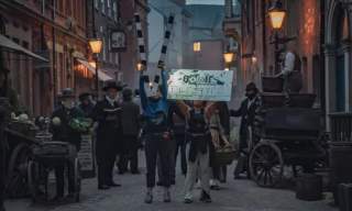 Set of High Street in Hull for Bodies TV show. Actors stand in costumes whilst set assistants hold up boards.