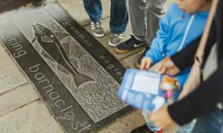 Stone plaque on Hull’s Fish Trail featuring an engraved fish illustration and species name, with visitors standing nearby while following the trail.