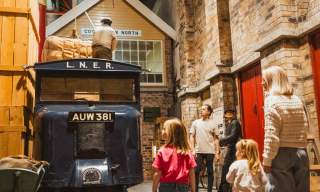 Families exploring a historic railway-themed gallery, looking at an L.N.E.R. vintage delivery truck, luggage display, and recreated station setting inside a Streetlife Museum Hull .