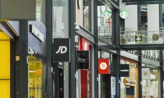 Interior view of St Stephens Shopping Center  featuring branded store signs including JD, Boux Avenue, Vodafone and Starbucks, with glass walkways, retail units and bright commercial displays.