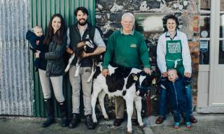 Group of 4 adults and 2 children standing in front of Broughgammon Farm with a calf at the front of the group.
