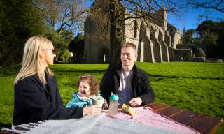 Family enjoying a picnic on a sunny day at a picnic table in front of Grey Abbey, County Down.