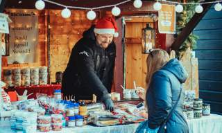 Mann som selger diverse delikatesser fra bod under julemarkedet i Sarpsborg. Foto.