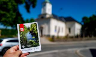 En hånd holder i en brosjyre for Borgleden foran en kirke