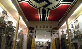 Inne fra museet med glassmontre med millitært utstyr og nasiflagg i taket