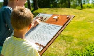 To gutter studerer plakater ved kulturminner - her gravhaug
