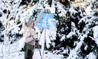 En dame børster av snøen på skiløypeskilt