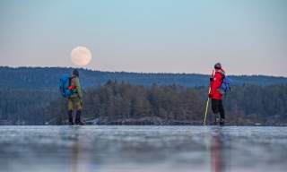 To menn på turskøyting med vakker måne på åskammen